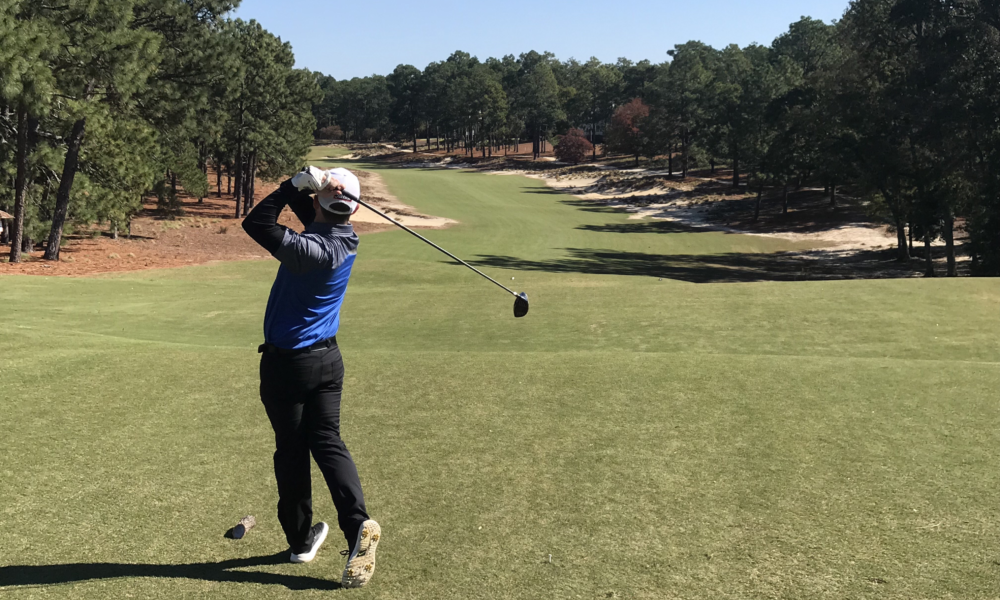 Golfer swinging club with course in background