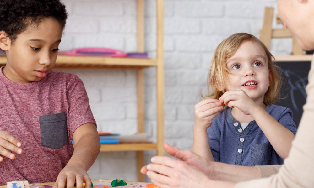 Two preschool aged children sitting with an adult